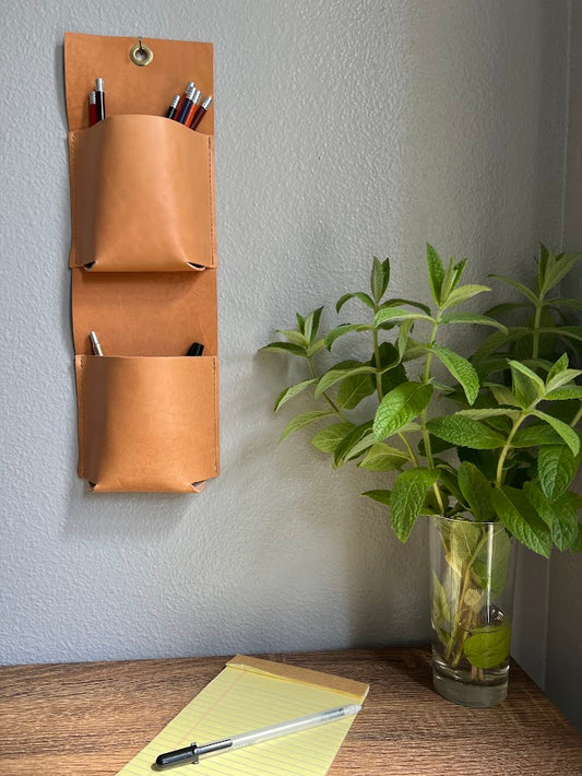 Stylish hanging organizer in nude leather, holds pens and art supplies.