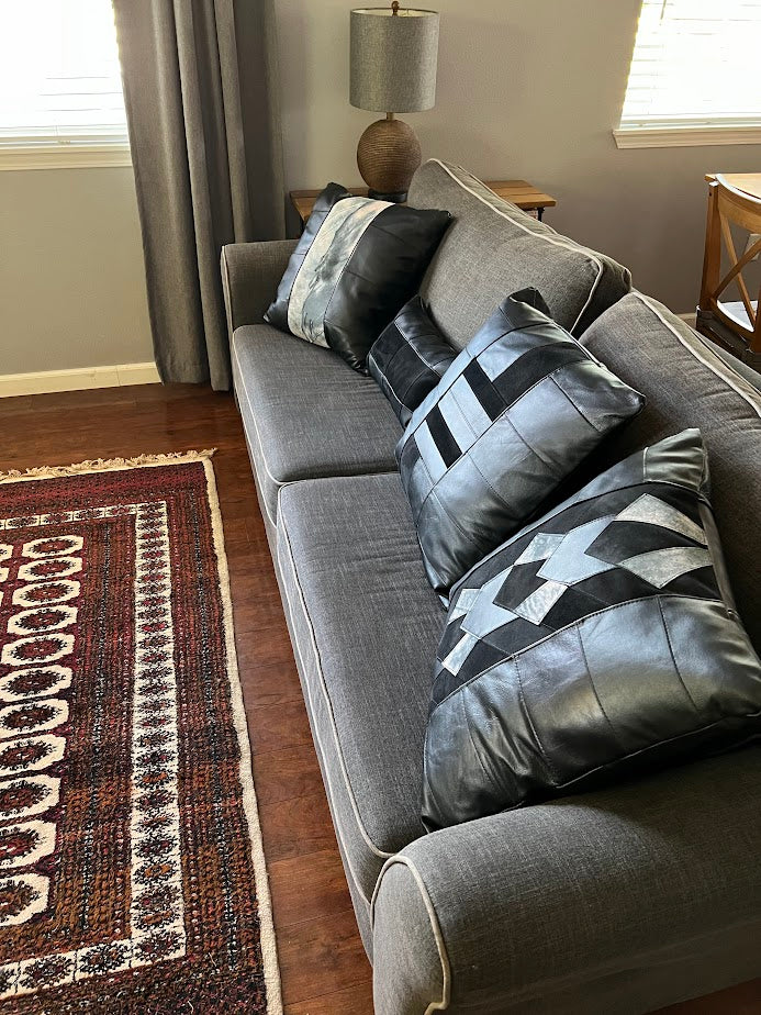 Assortment of black leather patchwork pillows on grey couch.