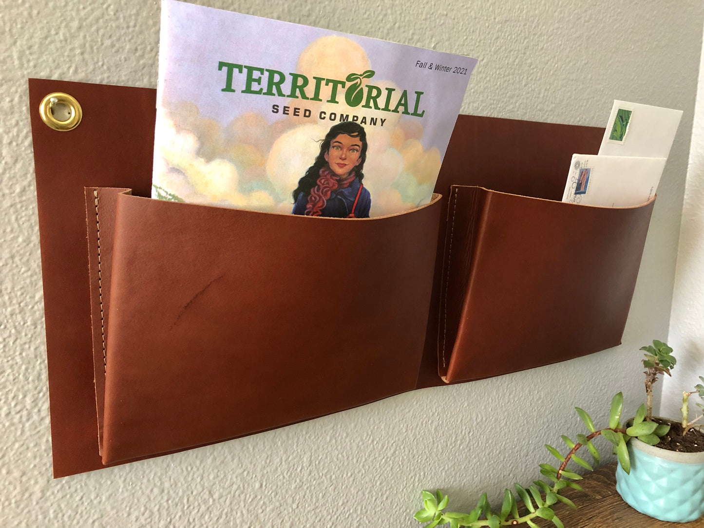 Close up of brown leather wall pockets; one holding mail, one holding a seed catalog.