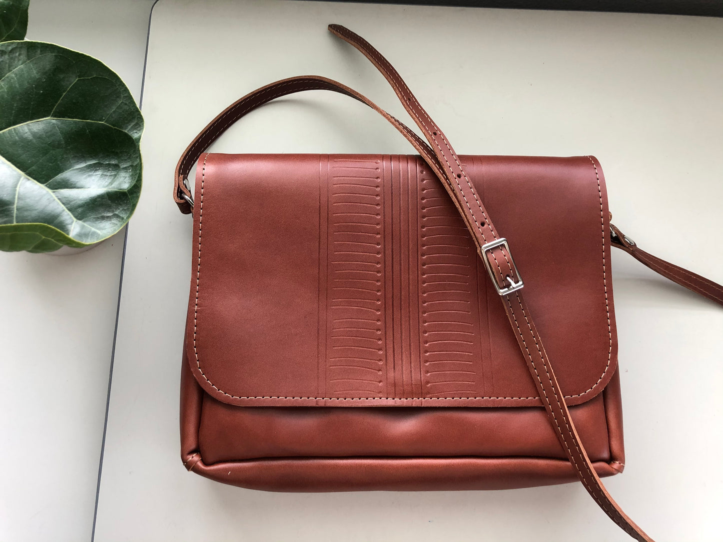 Buttery brown leather bag with hand tooled geometric detail, lies on table.