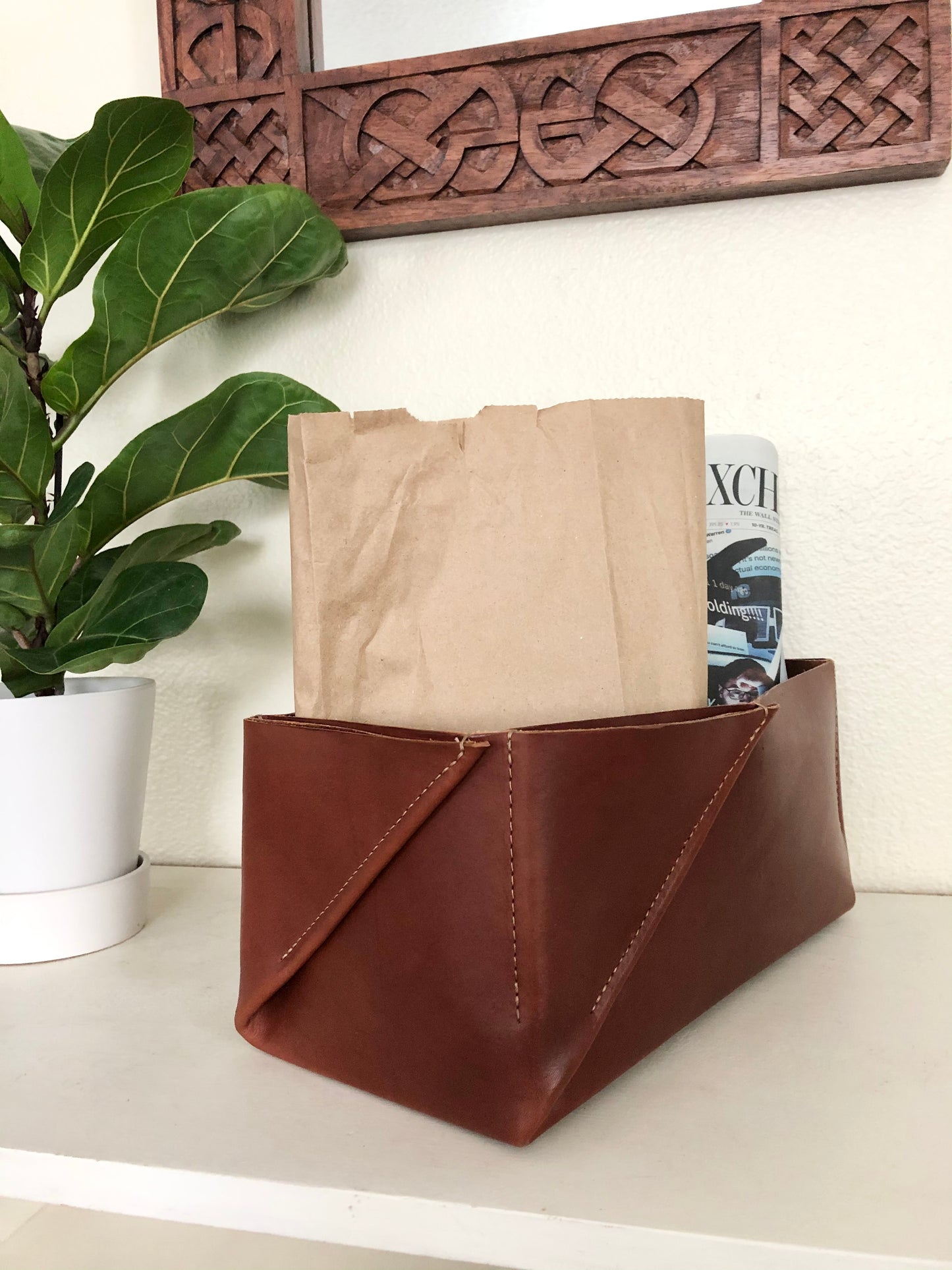 Rectangular leather box holds lunchbag and newspaper on stylish entryway table.