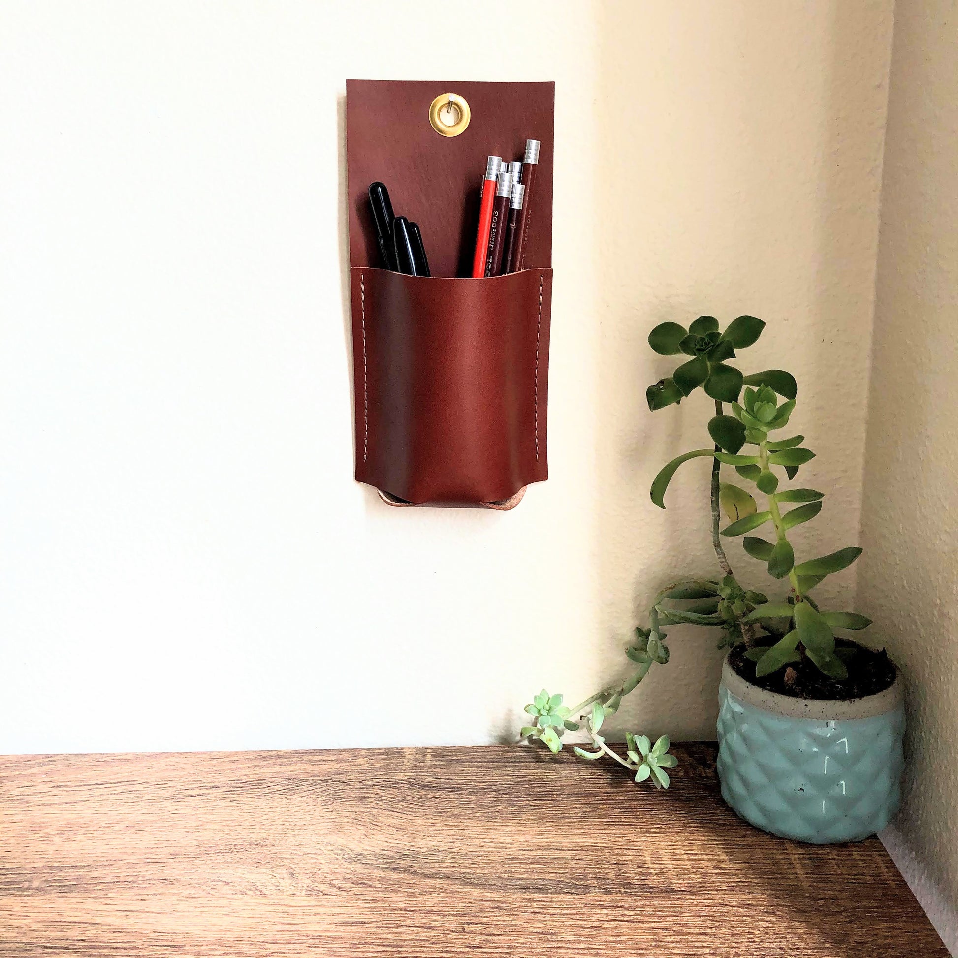 Small brown leather wall caddy holds an assortment of colorful pencils near an entry table.