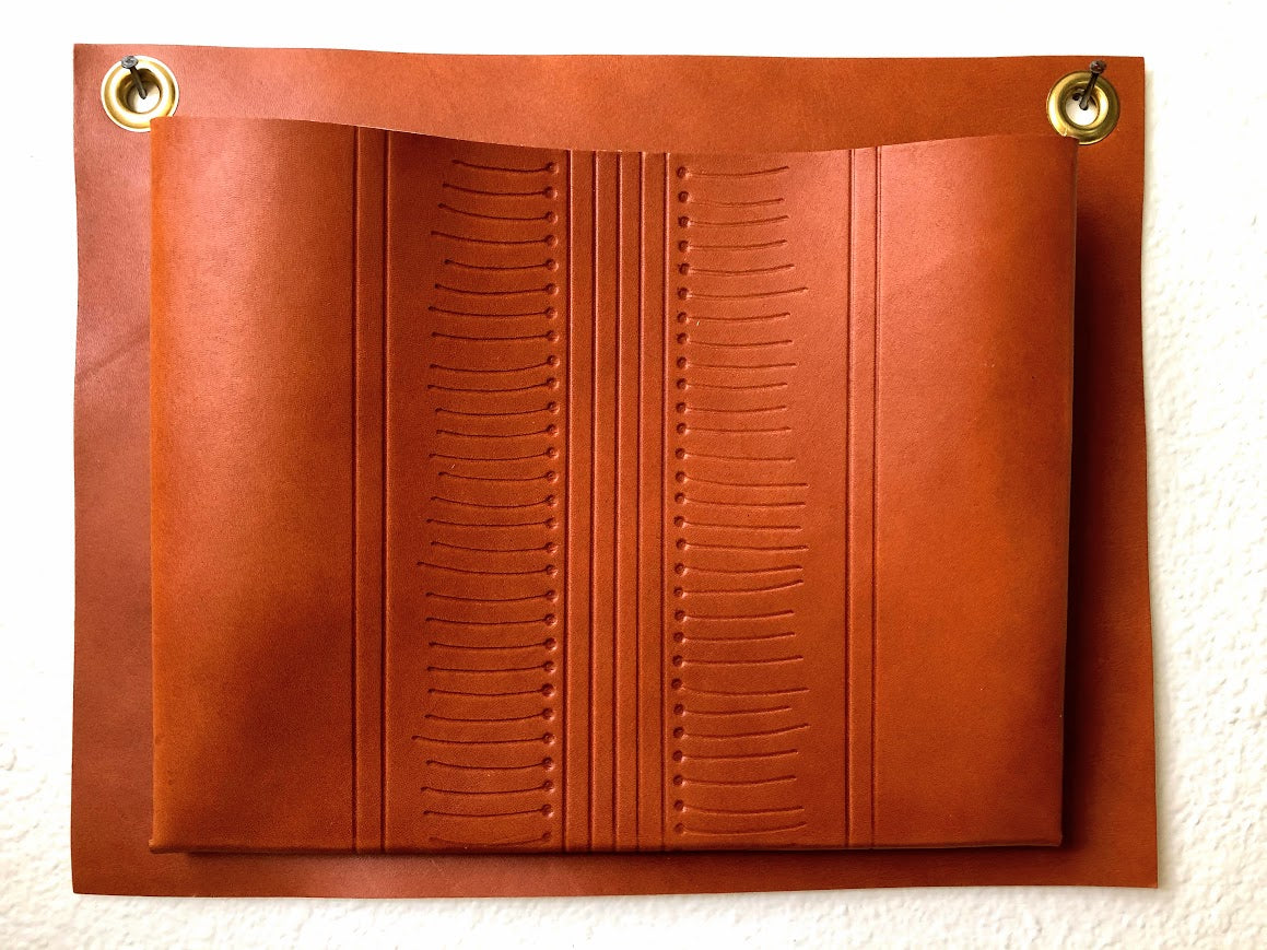 Tan, patterned, leather wall pocket hanging on wall.