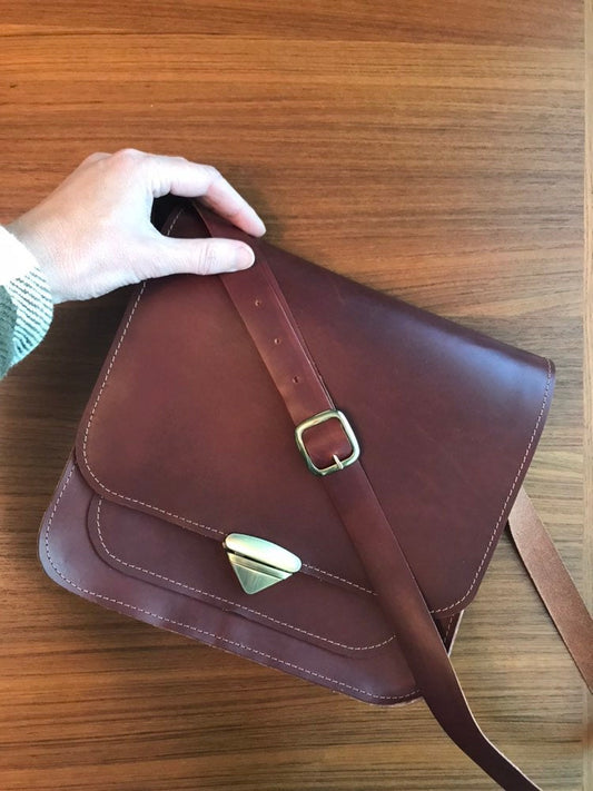 Hand holds structured brown leather messenger bag with triangle clasp