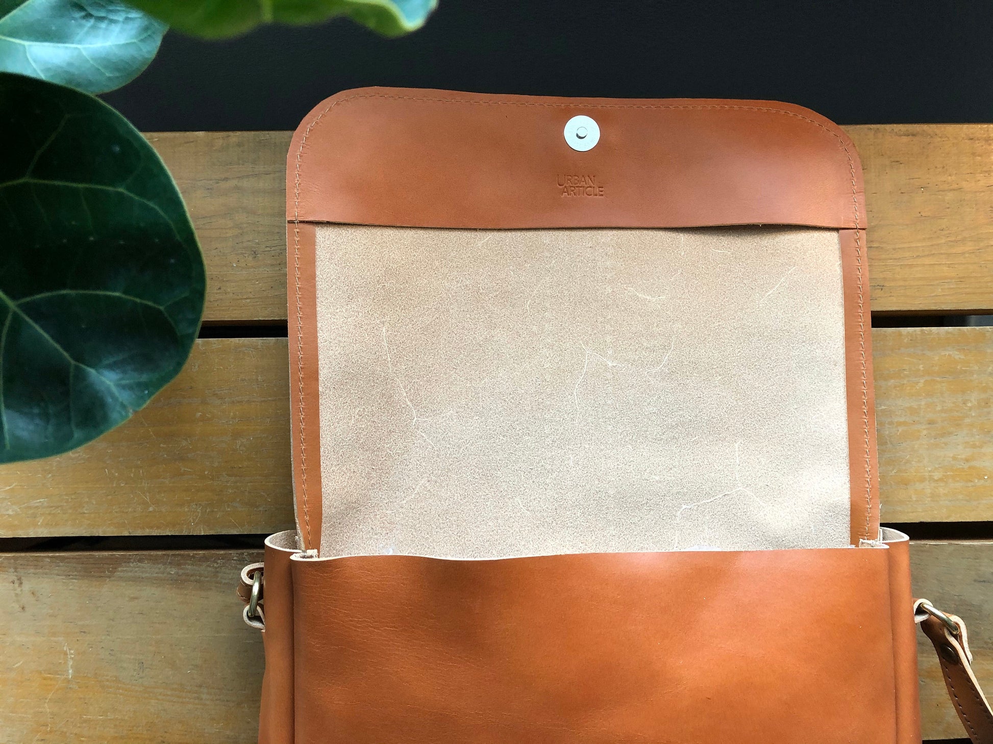 Tan leather crossbody bag opened to show natural leather interior and snap closure.