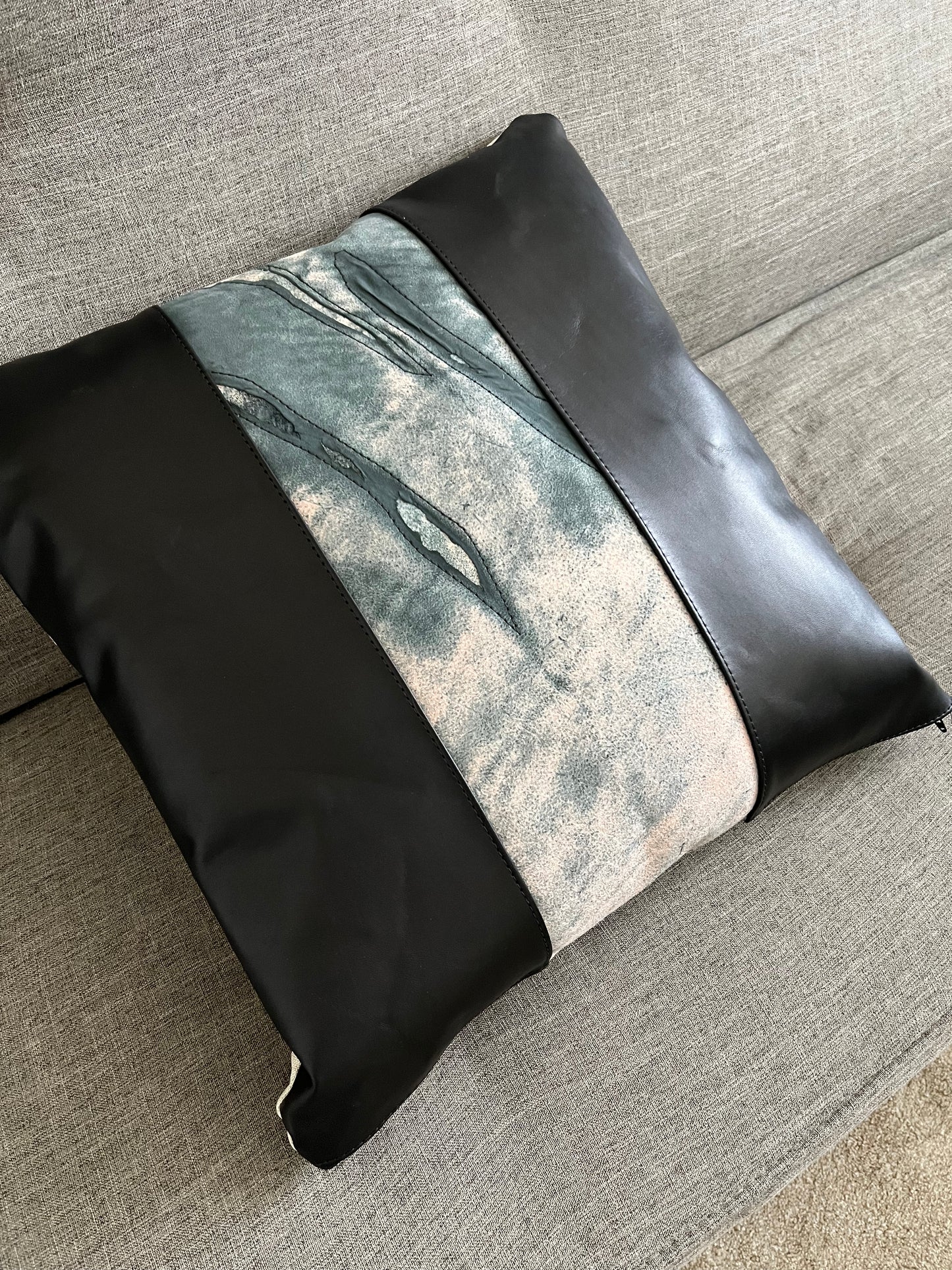 Modern, artsy, leather throw pillow in black and grey tones, rests on a grey couch.