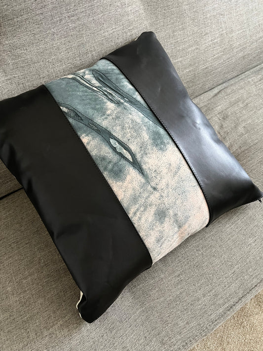Modern, artsy, leather throw pillow in black and grey tones, rests on a grey couch.