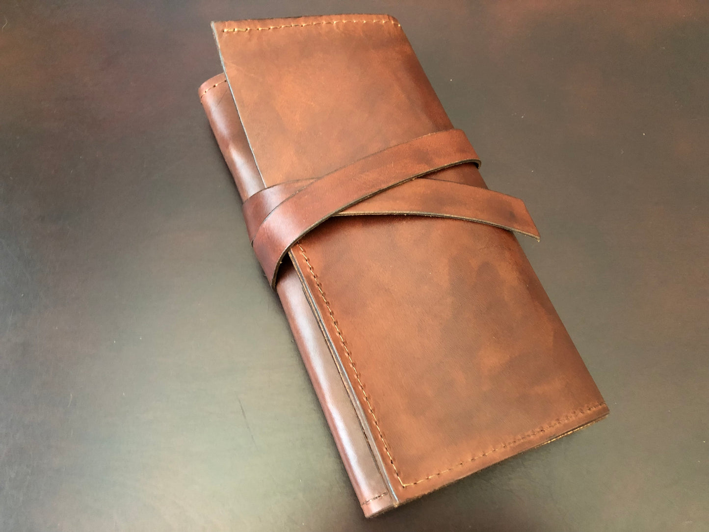 Handcrafted brown leather tool roll lies on table.