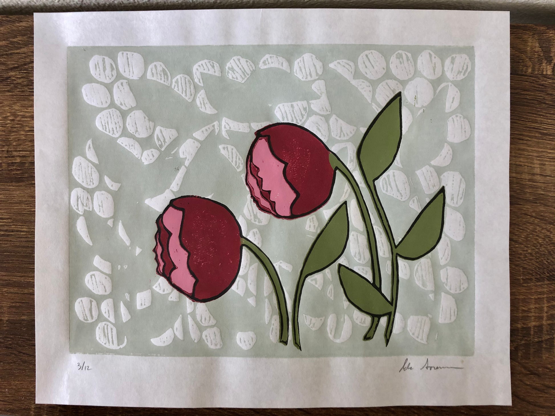 Two red and pink blooms pop from a soft green background in a lino print.