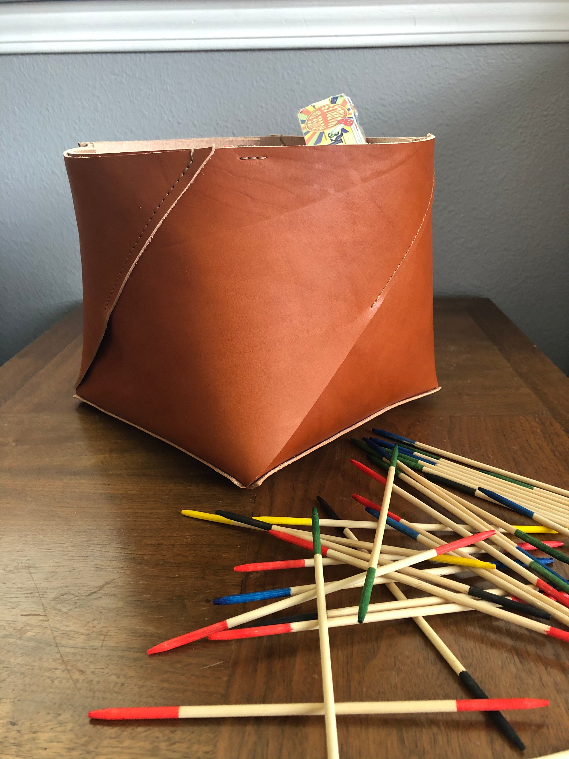 Handcrafted tan leather bin sits near a game of Pick up Sticks.