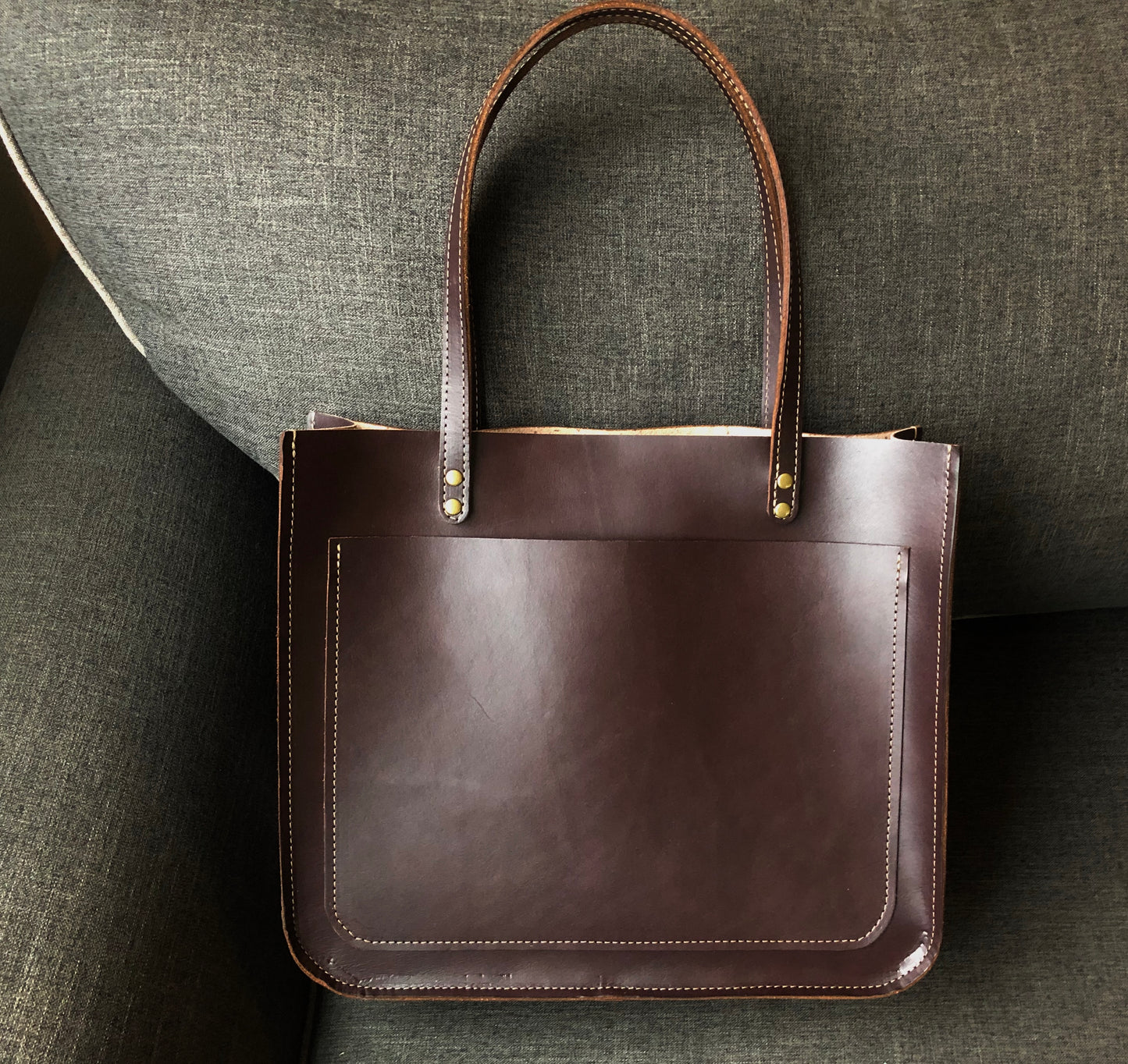 Rich brown leather tote bag sits on couch.