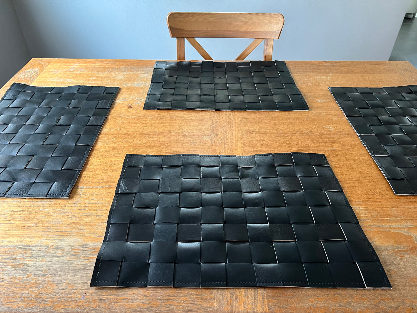 Woven black leather placemats gleam on a wooden table.