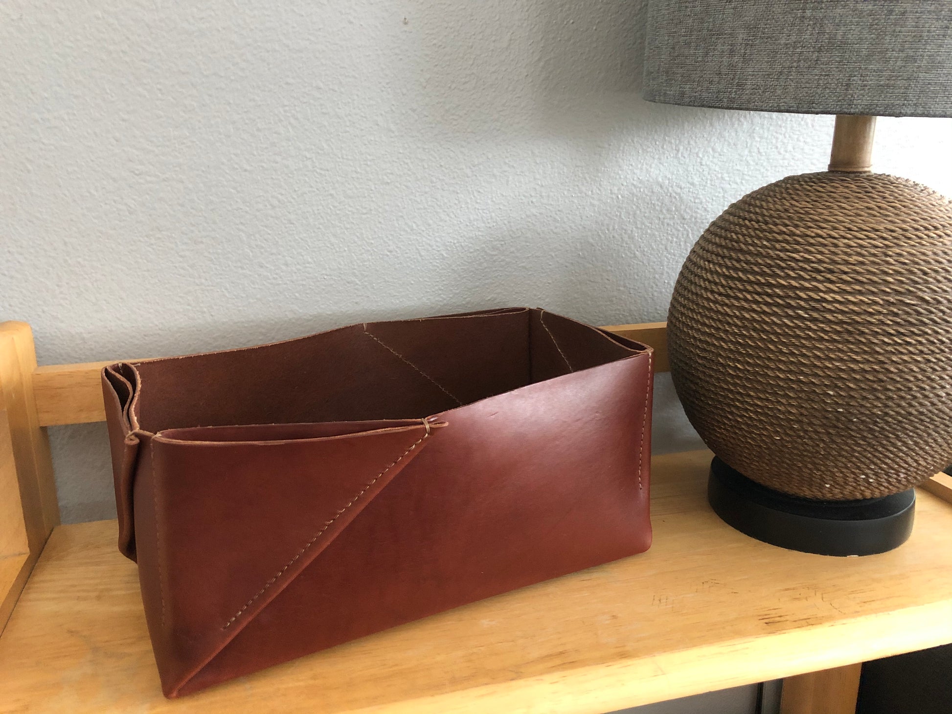 Folded leather box sits on shelf near rustic lamp.