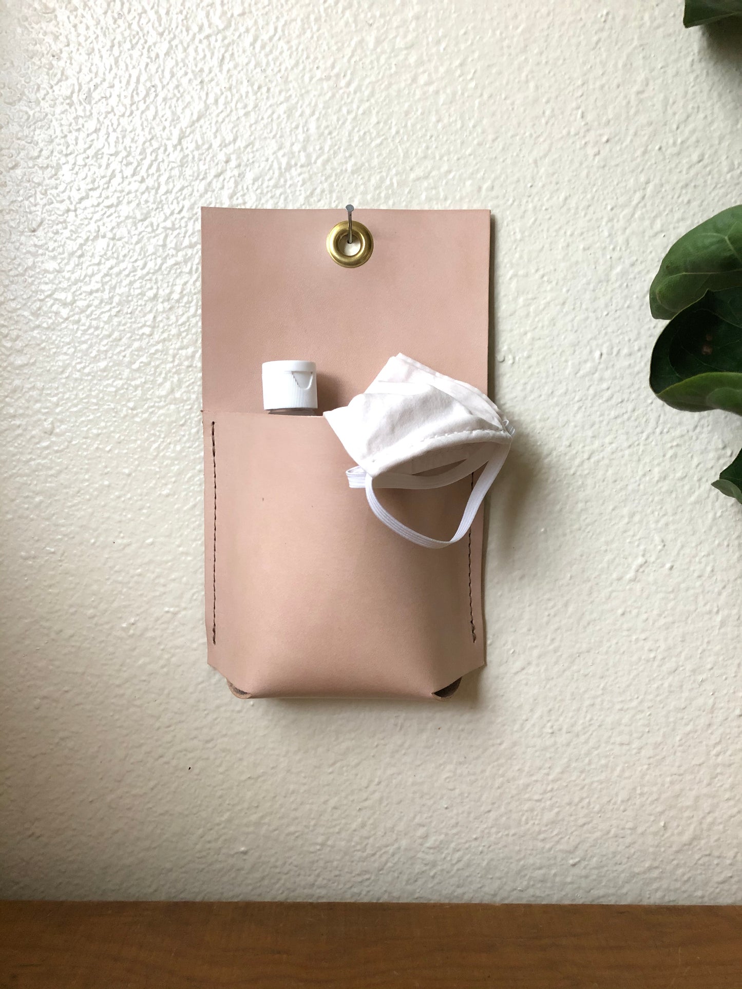 Nude leather wall pocket holds mask and sanitizer.