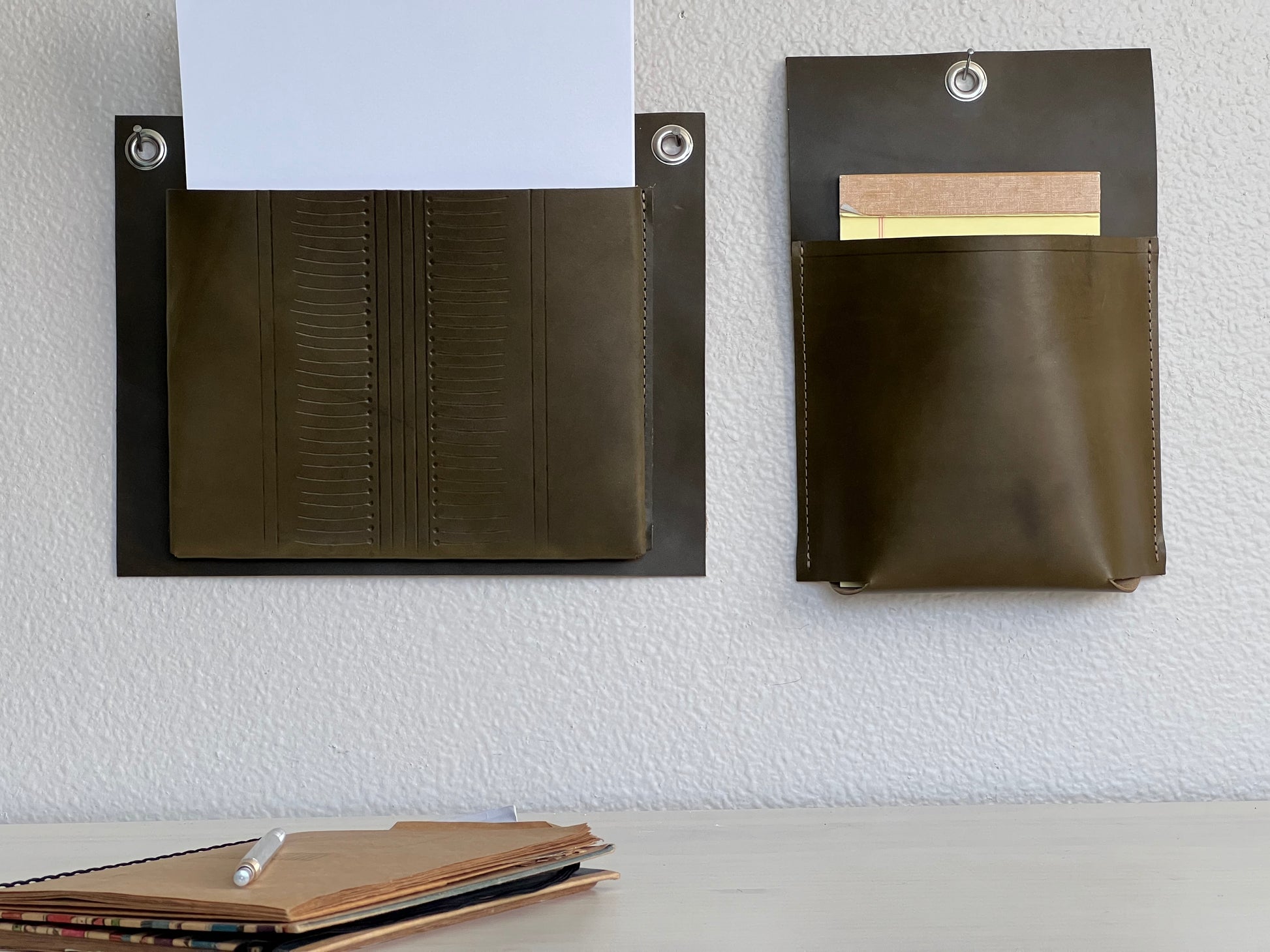 Olive green leather wall pockets hold paper above desk.