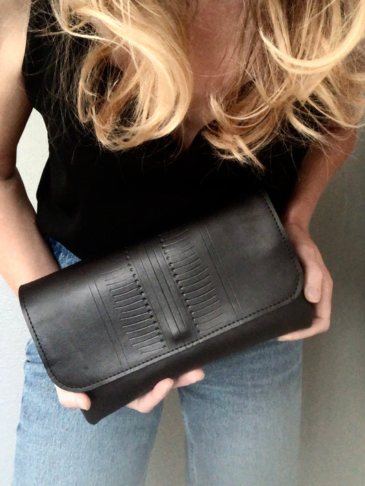 Woman holds black leather clutch with modern, hand-tooled pattern on the front.