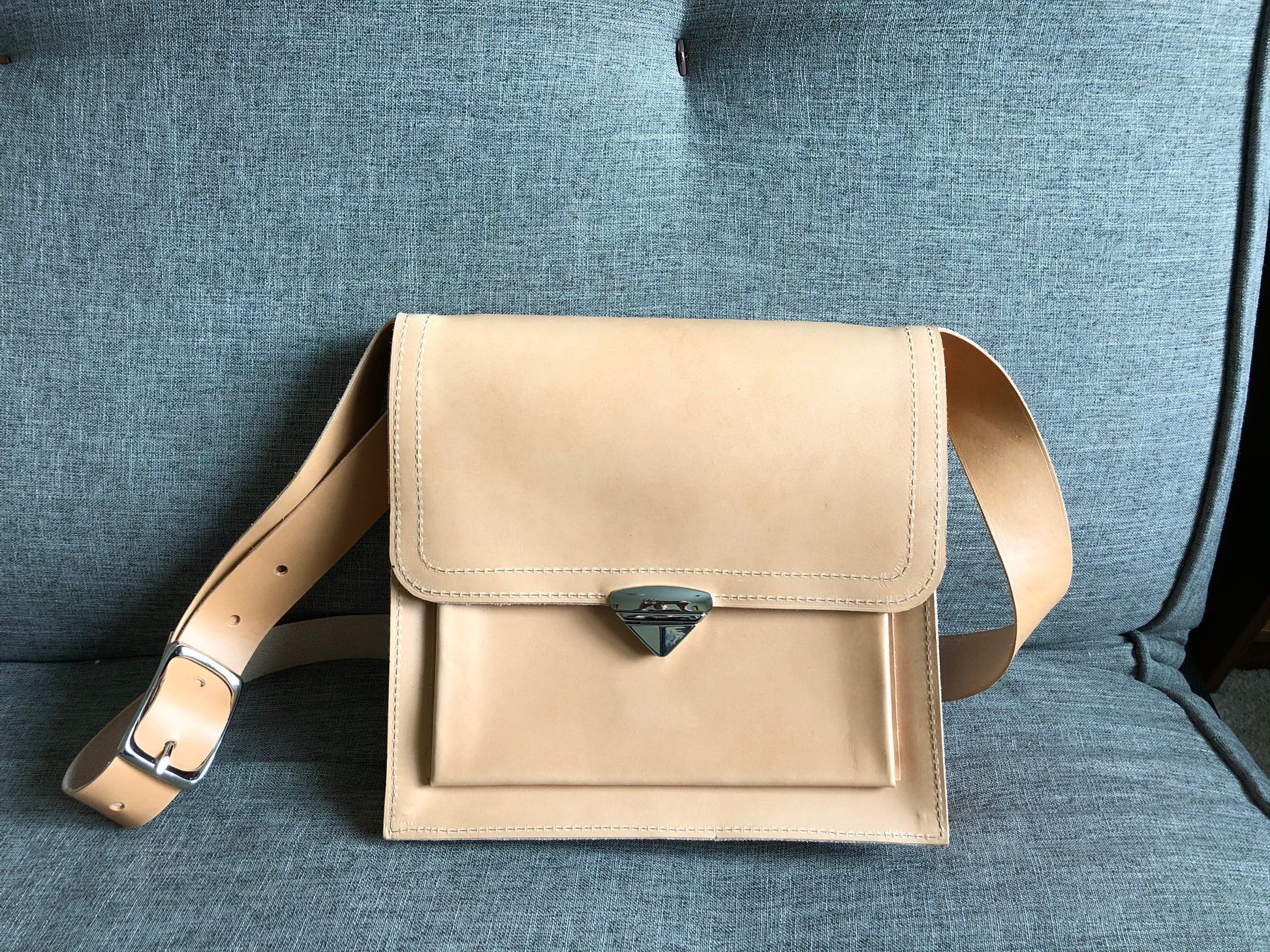Nude leather crossbody bag sits on a couch.