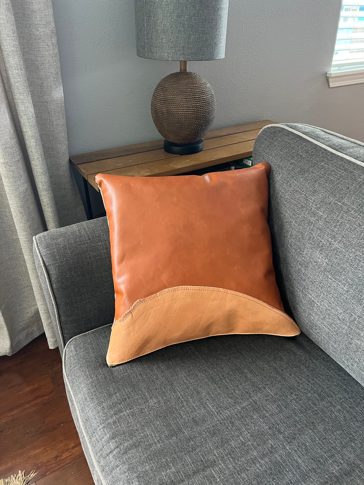 Two toned tan, leather pillow accentuates a modern, gray couch.