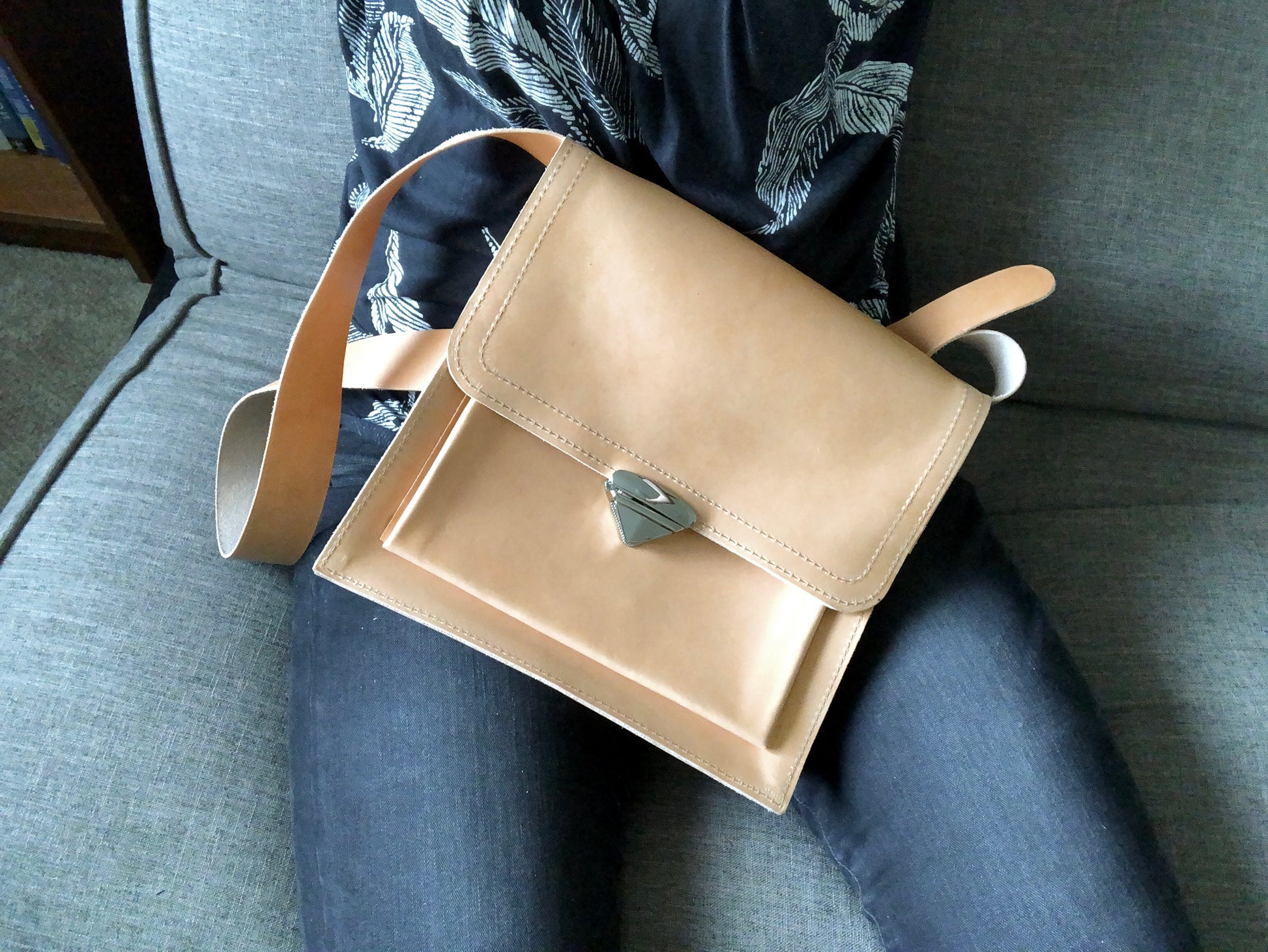 Buttery, nude leather messenger bag rests on a woman's lap.
