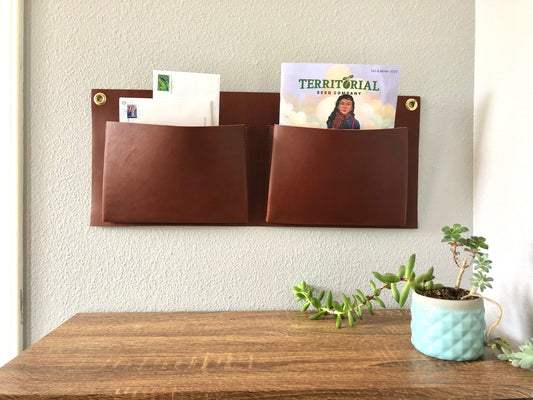 Brown leather wall pockets hold mail and a seed catalog over a clean table top with potted plant.