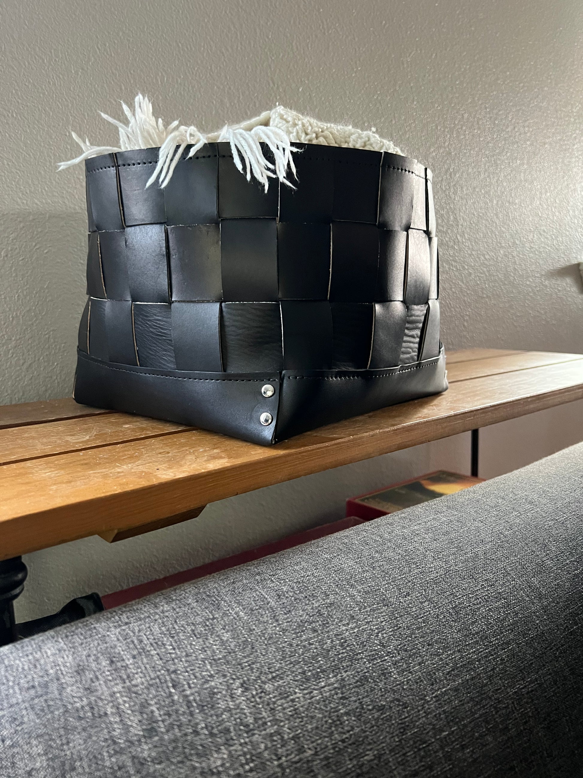 Woven leather bin holds a blanket near a couch.