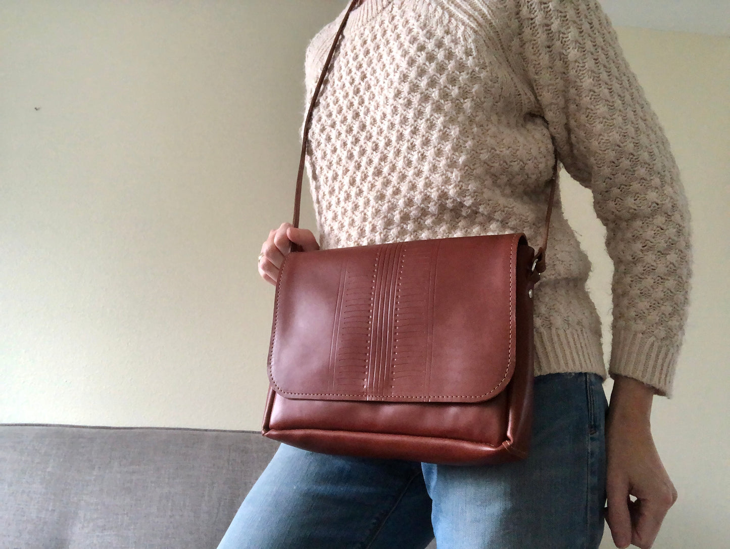 Woman wears brown leather bag with center pattern detail.