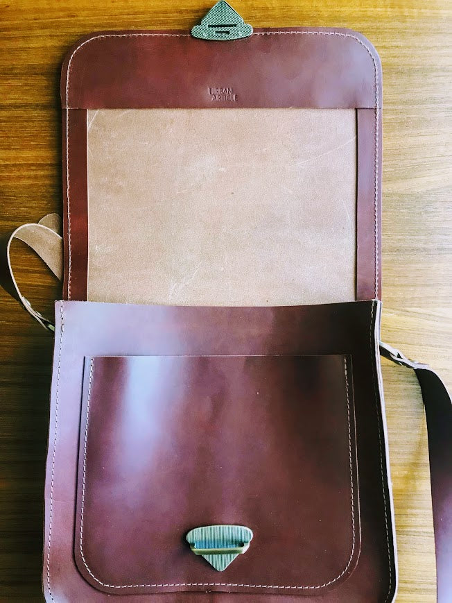 Brown leather purse lies opened on table showing front pocket and triangle closure.