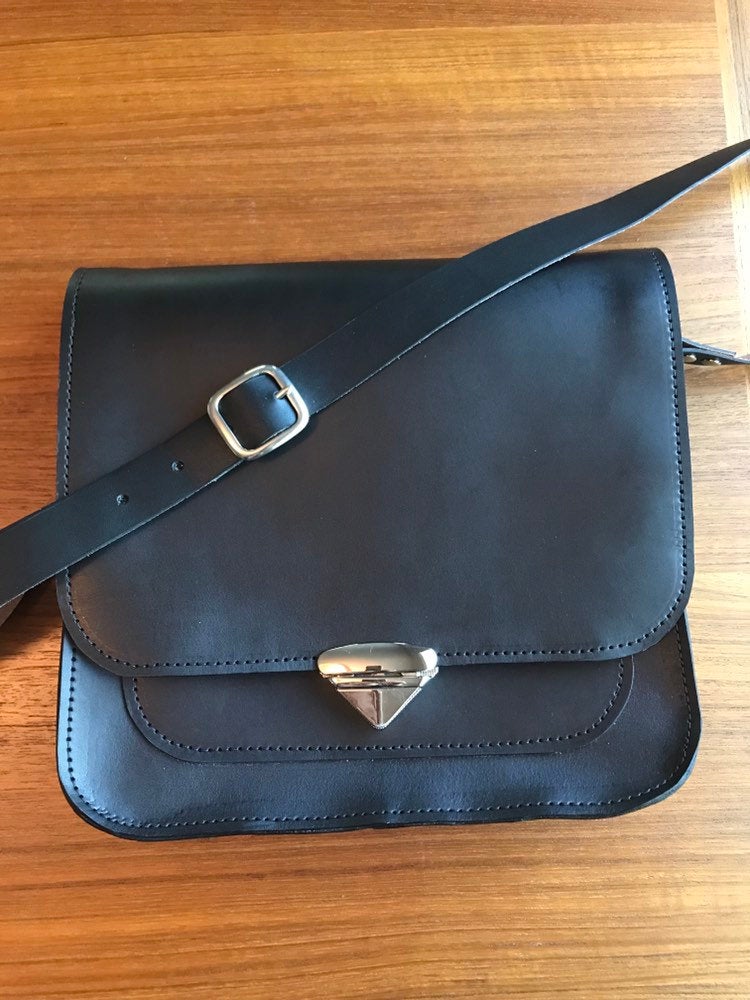 Structured black leather crossbody messenger bag lies on table