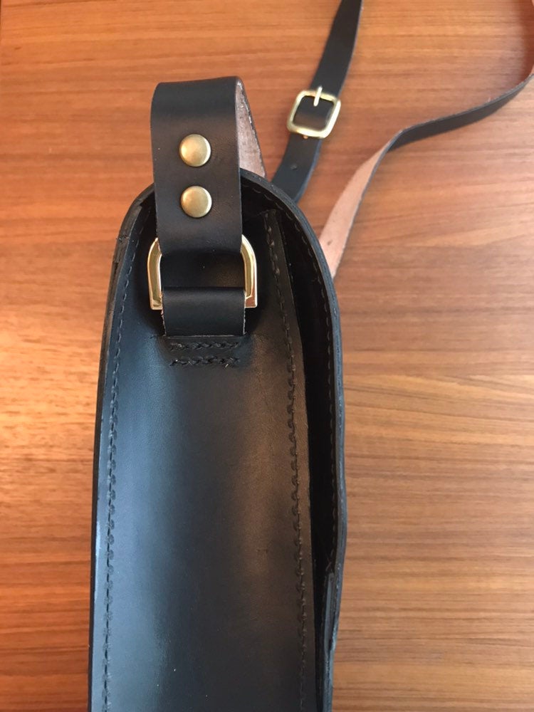 Side view of structured black crossbody bag showing strap hardware