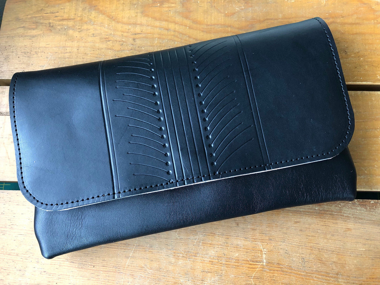 Black leather clutch with patterned design on front, sitting on a table