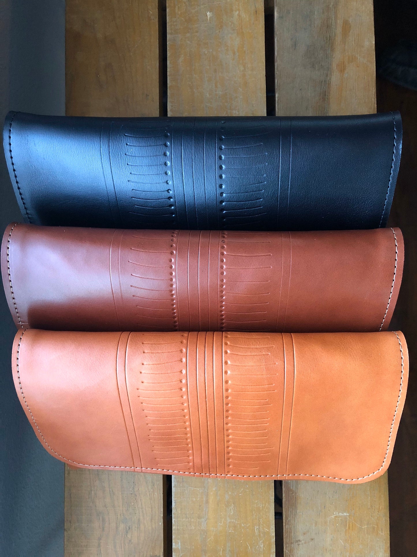 Row of three leather clutches, black, brown, and tan.