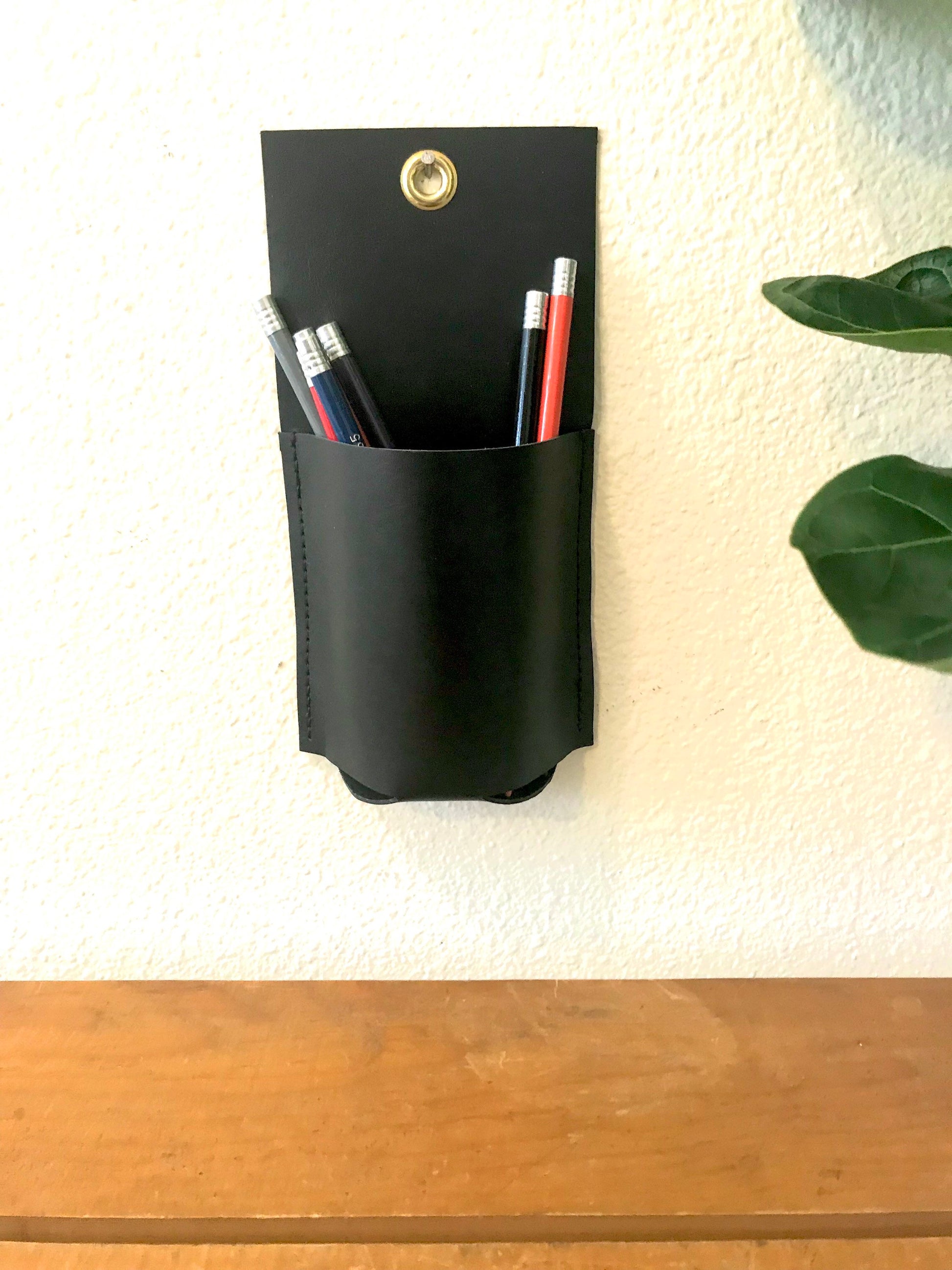 Small black leather wall caddy holds colored pencils above a wooden table