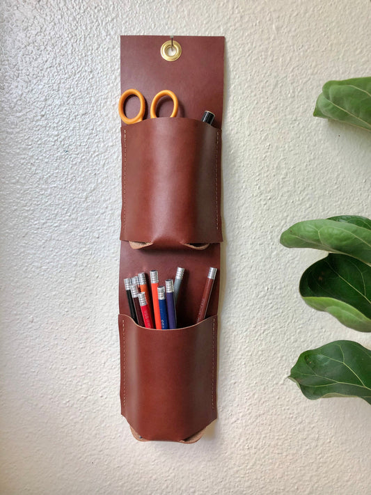 Brown two pocket vertical wall organizer holds scissors, pens, and colored pencils
